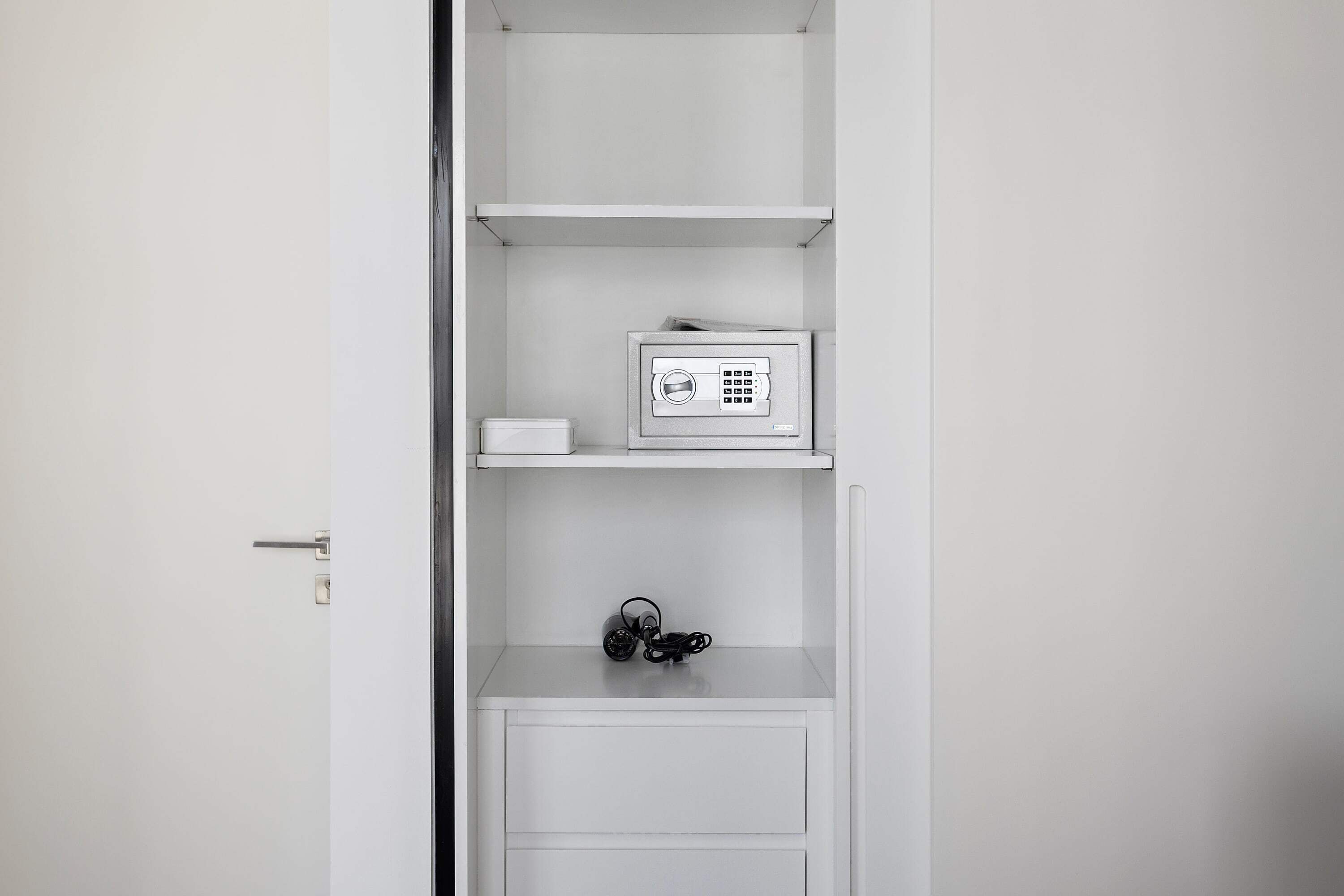 A white wardrobe with a small radio on the top shelf and a black object on the bottom shelf.