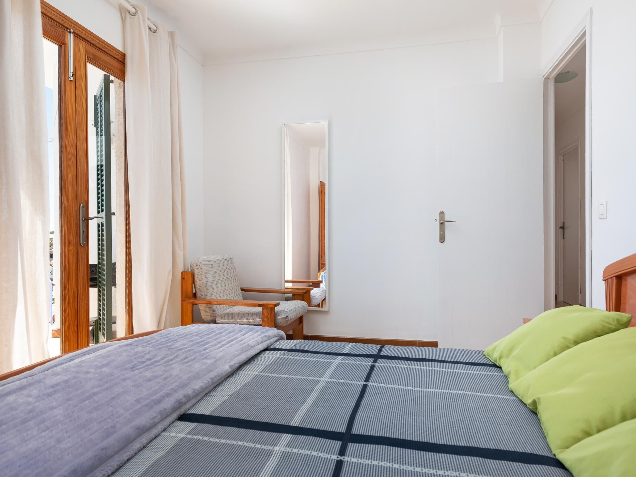 A bedroom with a bed, a chair, a small table, and a mirror.