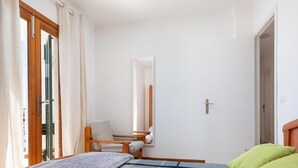 Een slaapkamer met een bed, een stoel, een klein tafeltje en een spiegel.