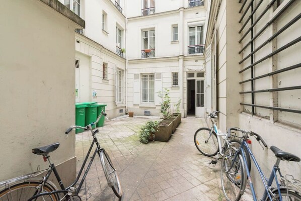 Stroll through this charming urban courtyard, surrounded by residential buildings with balconies and windows, and enjoy the lush greenery of the potted plants and garden area.