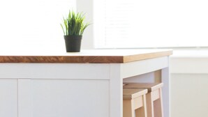 Un meuble blanc avec un plan de travail en bois et une plante en pot.