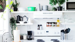 Une cuisine moderne avec des armoires blanches, un évier en acier inoxydable, une cuisinière et un four à micro-ondes. On y trouve divers ustensiles de cuisine et des plantes sur les plans de travail.