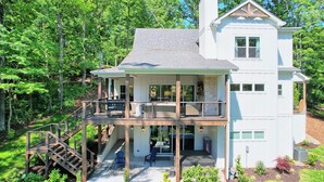 A two-story house with a balcony, a covered porch, and a staircase leading to the upper level. - Big Oak Bungalow by Chatuge Home Concierge | Lake House · Private Dock · Hot Tub · Ping Pong · Fireplace (Hiawasee)