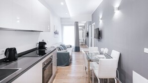 Een moderne keuken met witte kasten, een zwarte waterkoker en een eethoek met een glazen tafel en witte stoelen.
