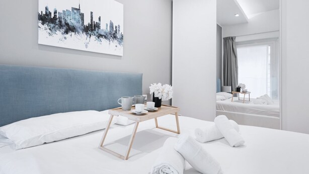 Een moderne hotelkamer met een groot bed, een stadsgezicht op de muur, een nachtkastje met een tray toiletartikelen, en uitzicht op de stad door het raam.
