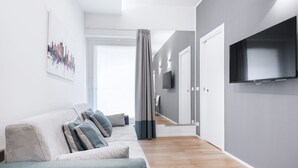 Een moderne woonkamer met een bank, een flatscreen televisie en een gang die leidt naar een trap.