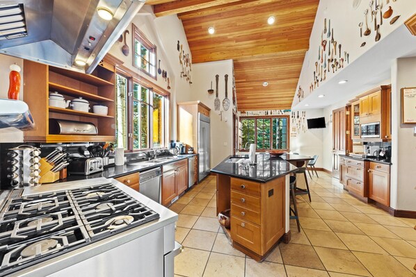 A spacious kitchen with a central island, wooden cabinets, and a stainless steel stove. - Chateau Hadarian (Vail)