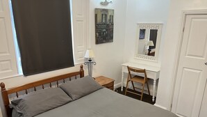 A bedroom with a bed, a desk, a chair, a lamp, and a mirror.