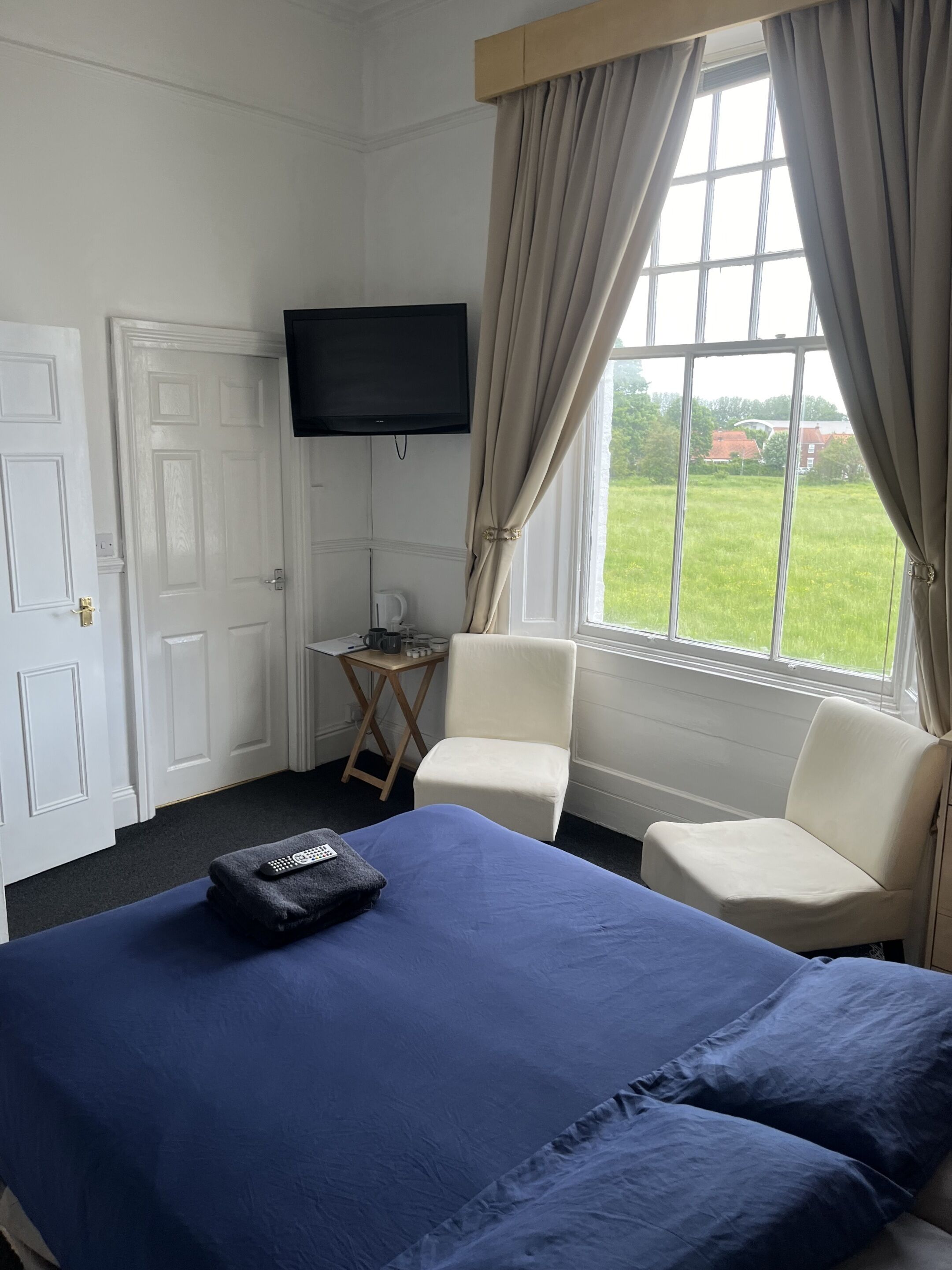 Una habitación de hotel con una cama, dos sillas, un televisor y una ventana con cortinas.