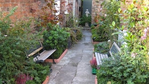 A narrow brick alley with benches and potted plants on either side.