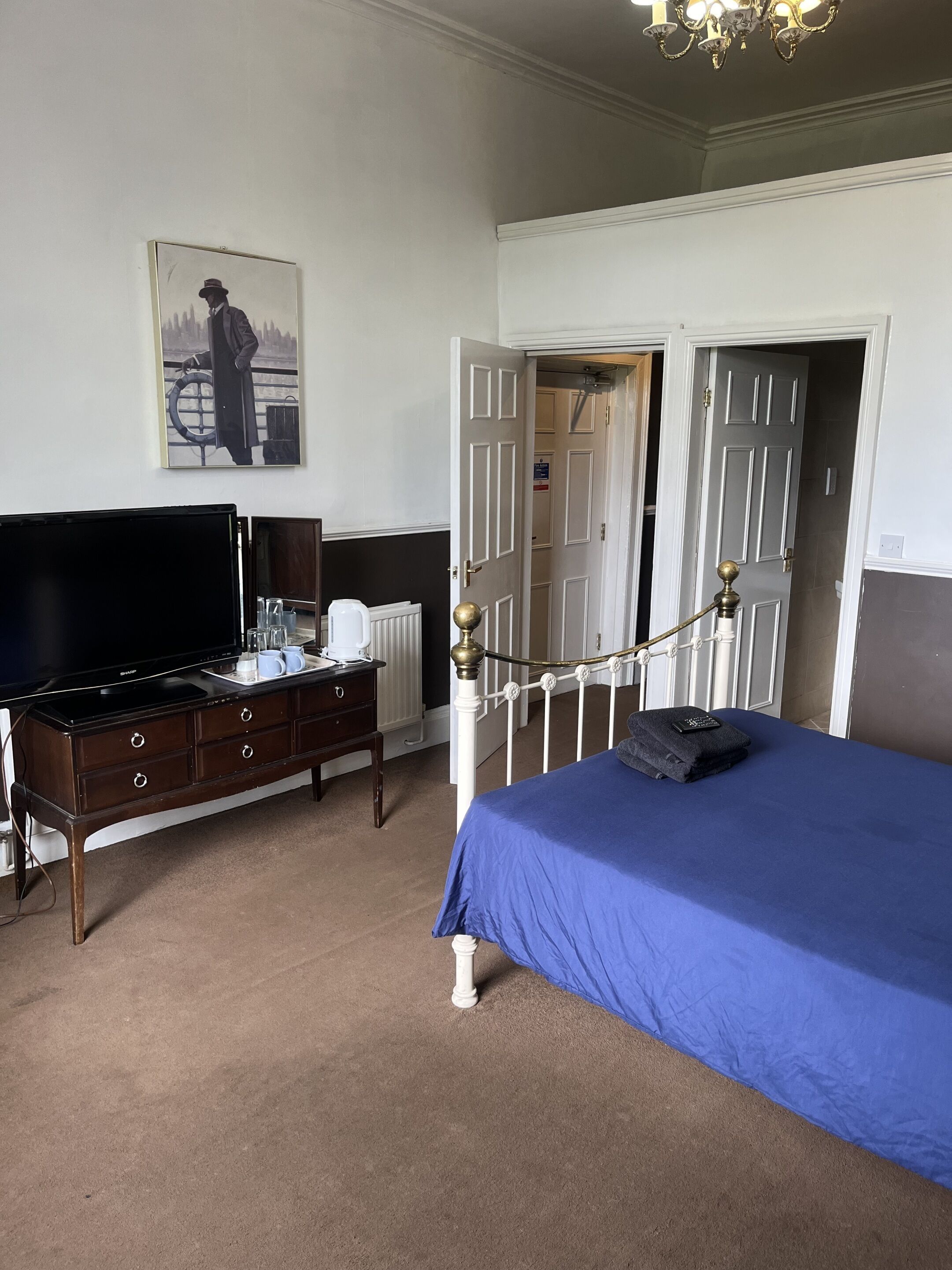 A bedroom with a bed, a dresser, a television, and a door leading to another room.