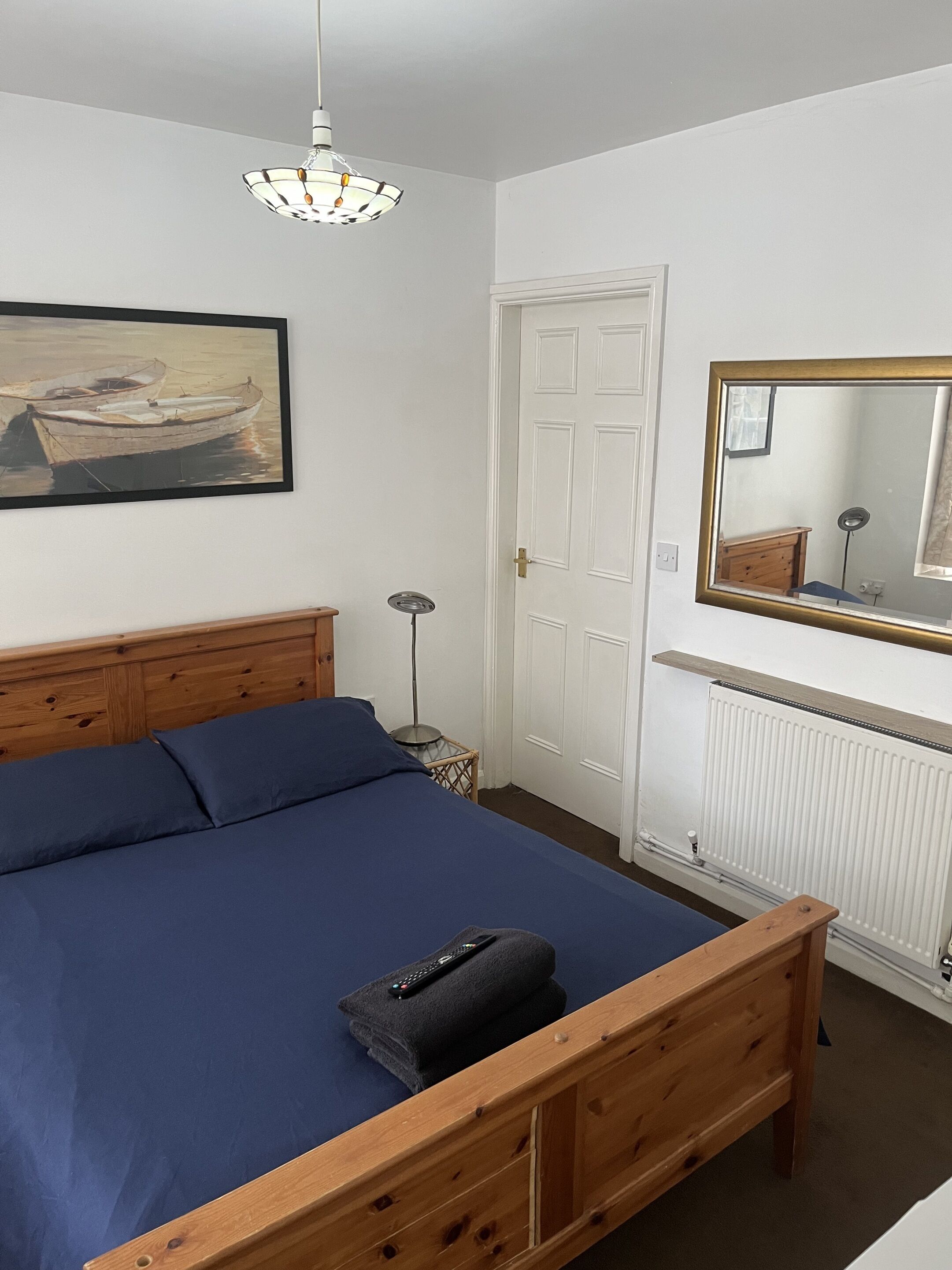 A bedroom with a wooden bed, a painting, a white door, a mirror, and a radiator.