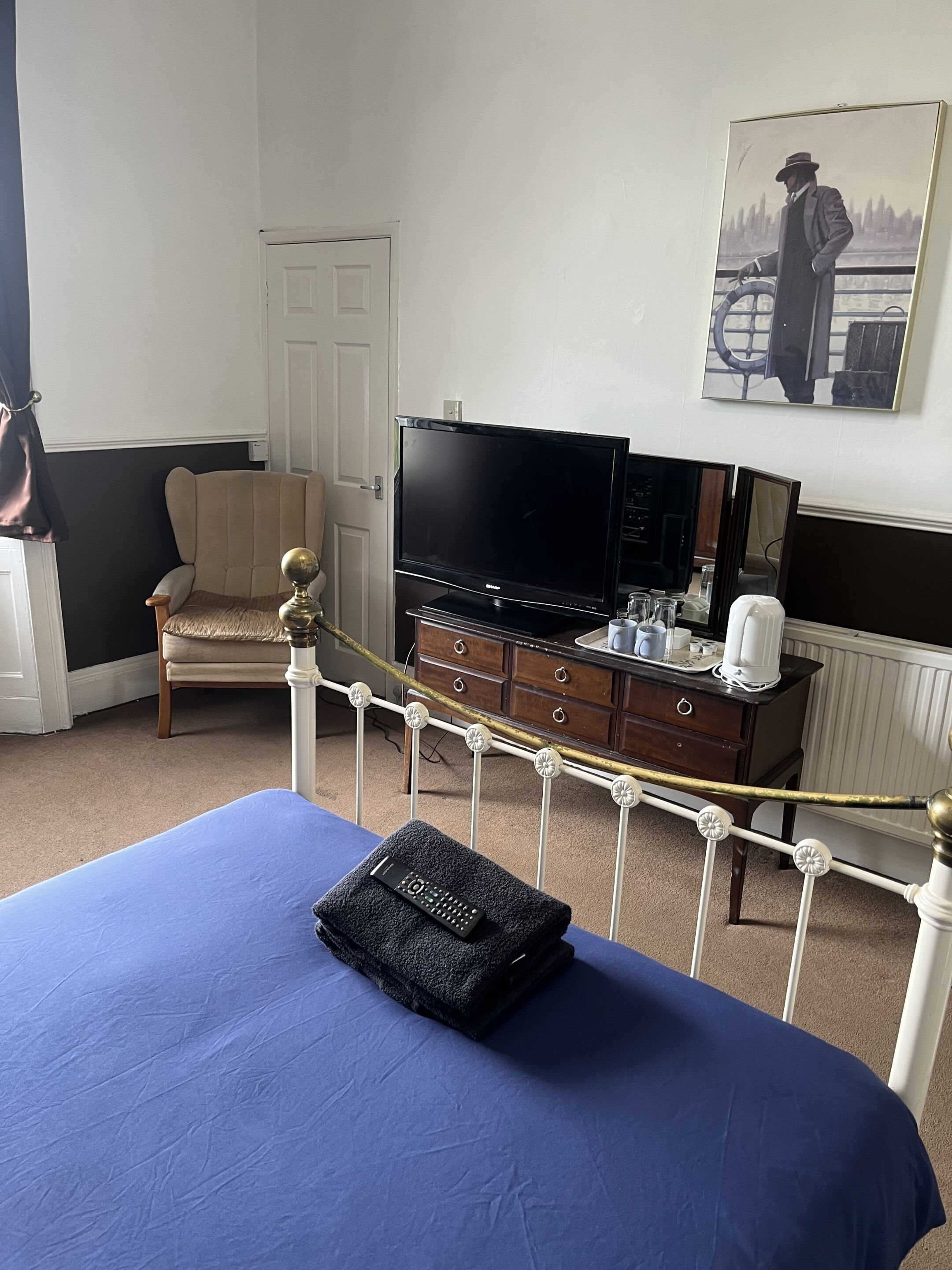 A hotel room with a bed, a television, a chair, a dresser, and a painting on the wall.