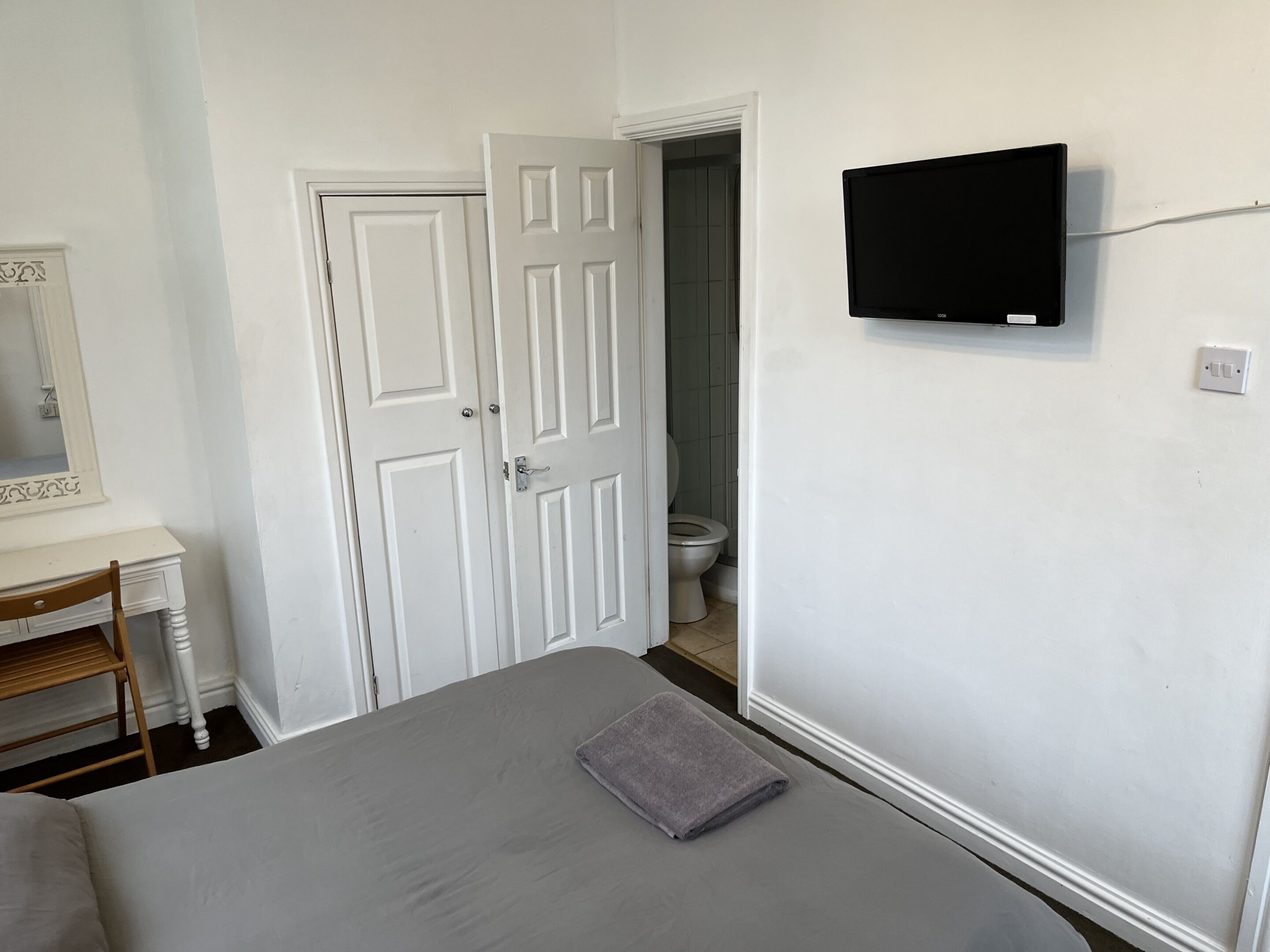 Un dormitorio con una cama, un televisor montado en la pared, una puerta y un baño pequeño visible a través de la puerta.