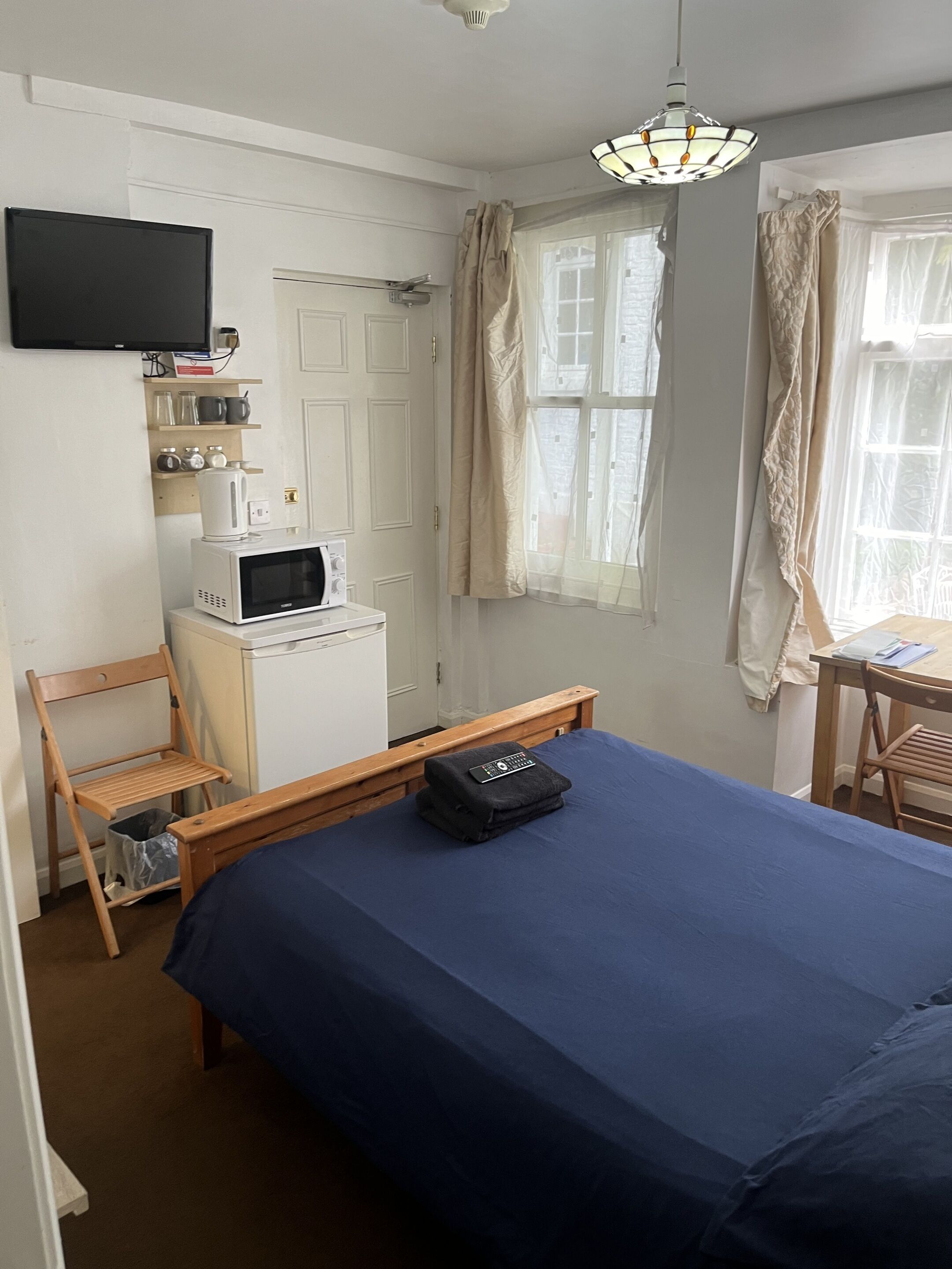 A bedroom with a bed, a desk, a chair, a microwave, a television, and a window with curtains.