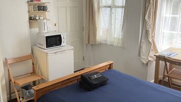 A bedroom with a bed, a desk, a chair, a microwave, a television, and a window with curtains.