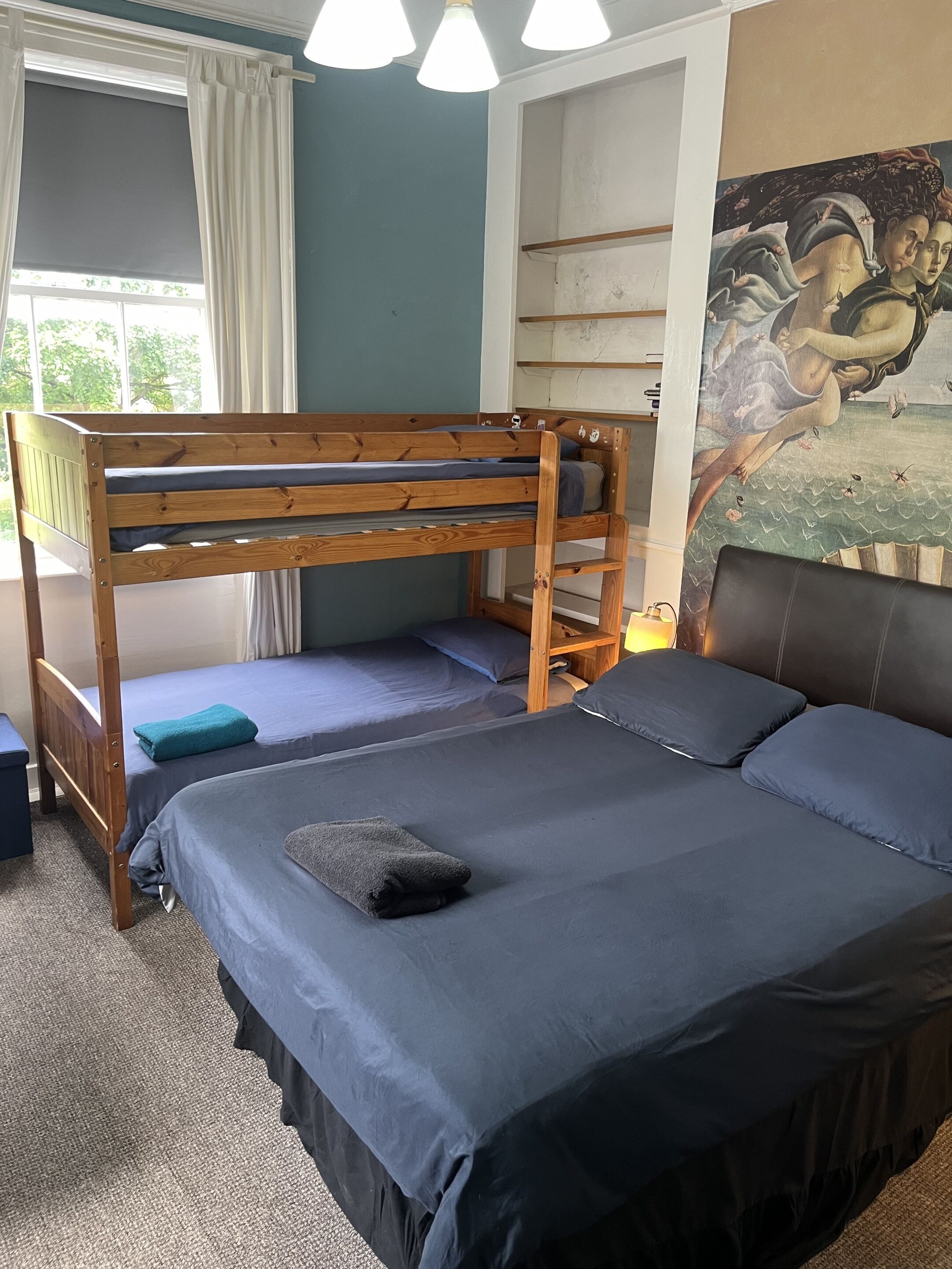 Ein Zimmer mit Etagenbetten, einem großen Fenster mit Vorhängen, einem Bild an der Wand und einem Teppichboden.