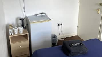 Habitación de hotel con cama, escritorio con cafetera, televisor montado en la pared y puerta con señal de procedimiento de emergencia.