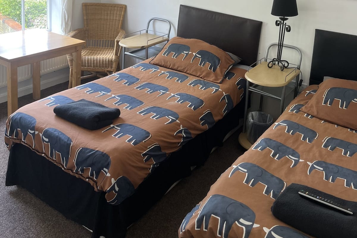 A hotel room with a bed, a chair, a table, and a lamp.