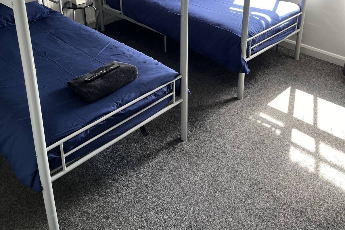 A dormitory room with bunk beds, a window with curtains, and a remote control on the lower bunk.
