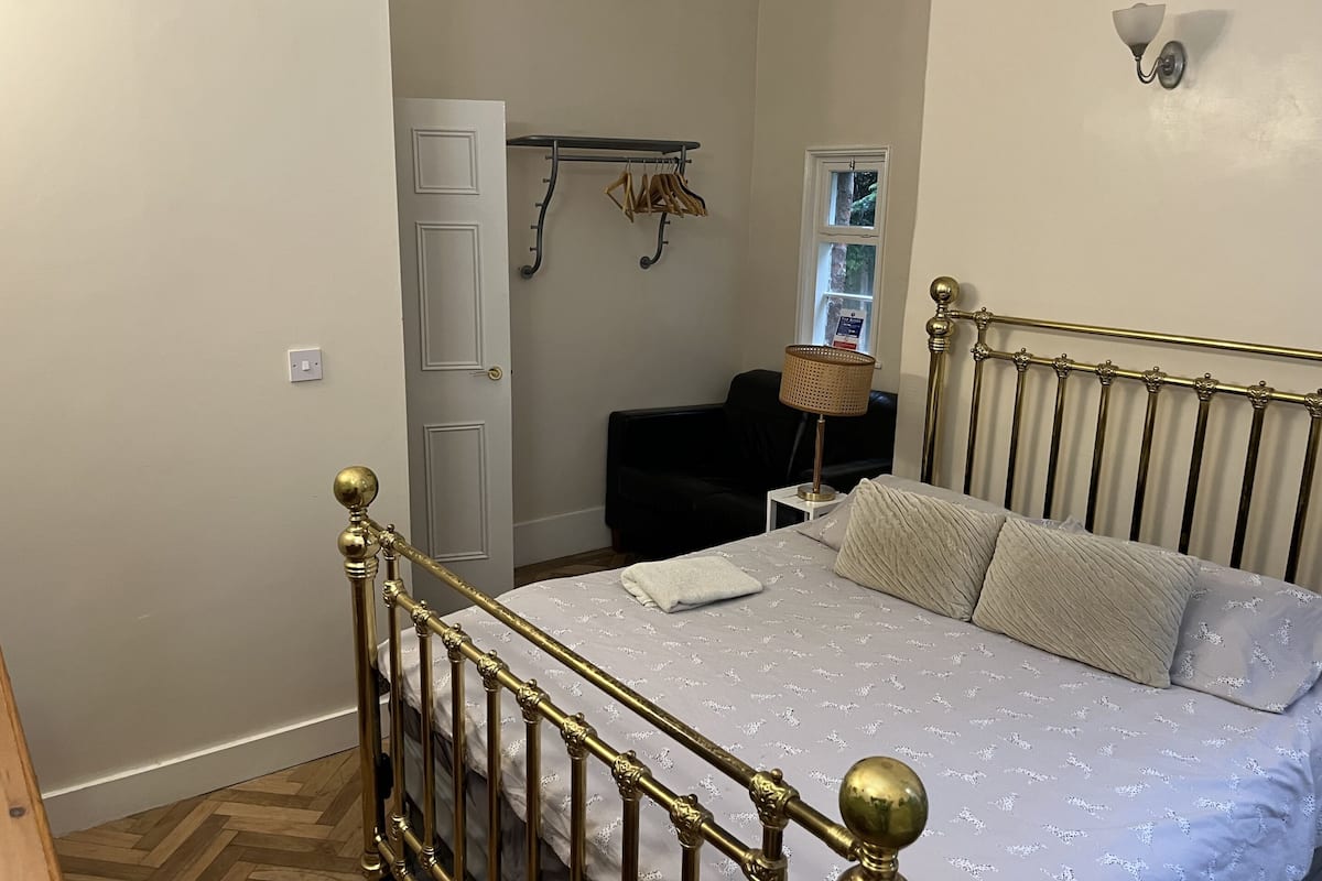 A bedroom with a bed, a radiator, a wall-mounted light fixture, a window, and a coat rack.