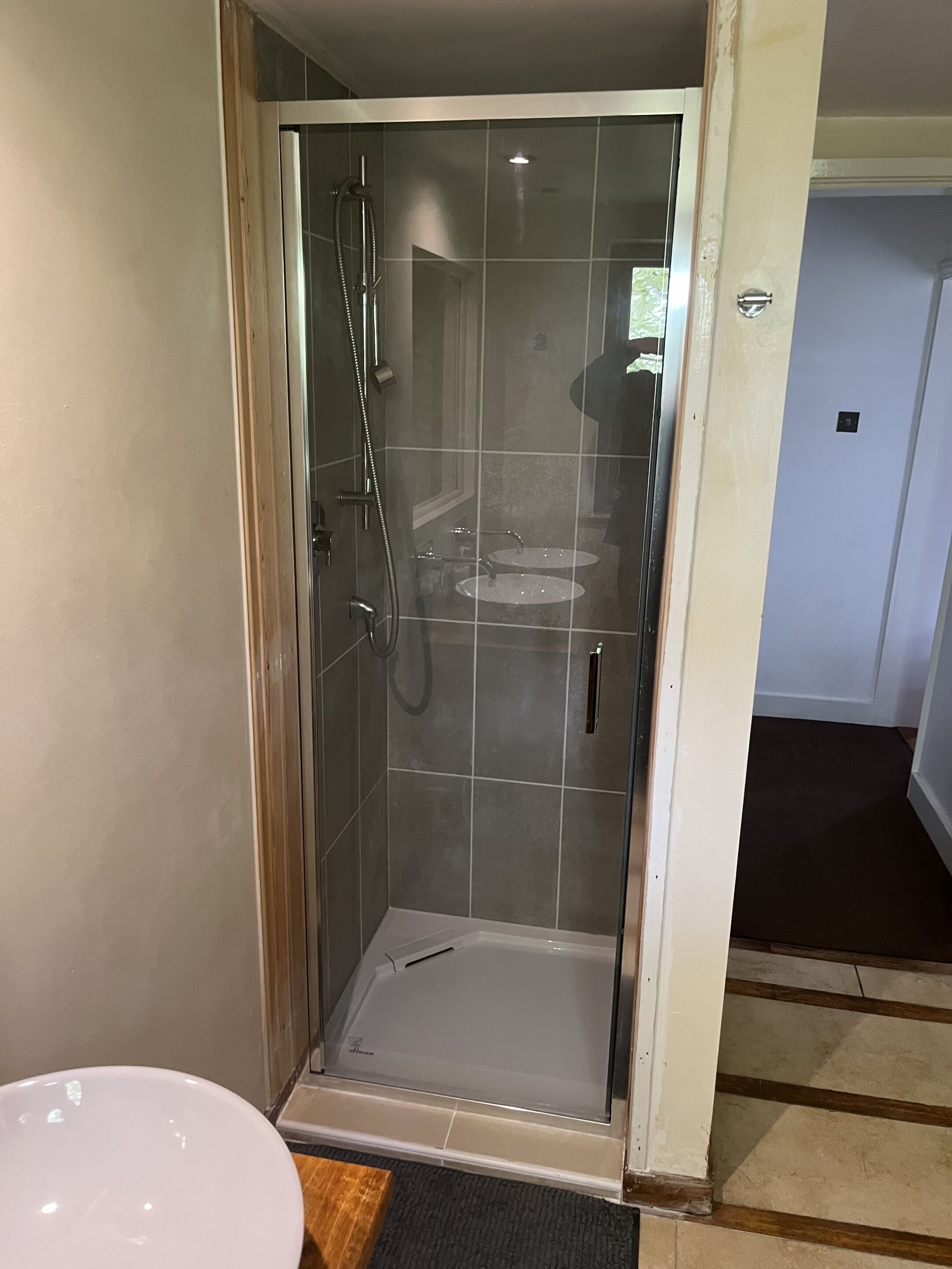 A glass-enclosed shower with a white sink and a handheld showerhead.