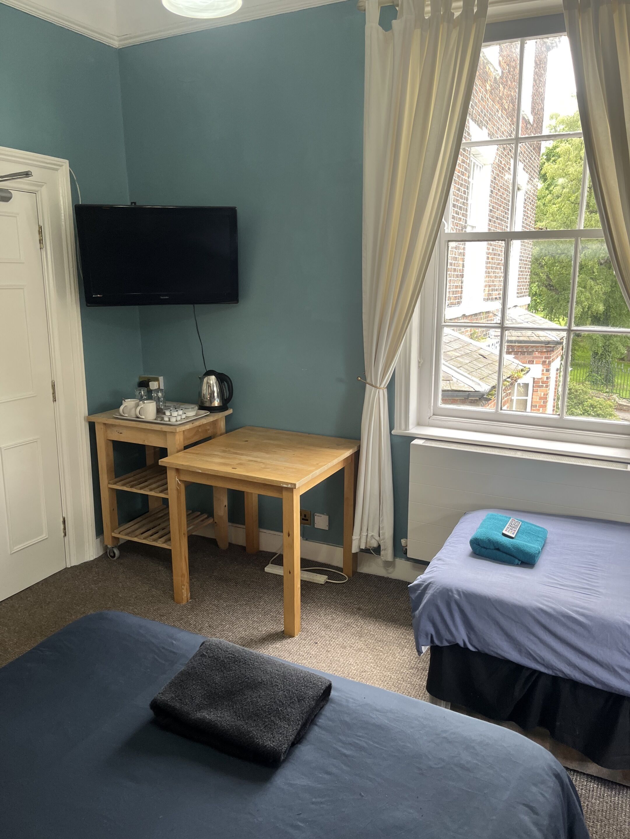 Una habitación con dos camas, un escritorio, un televisor y una ventana con cortinas.