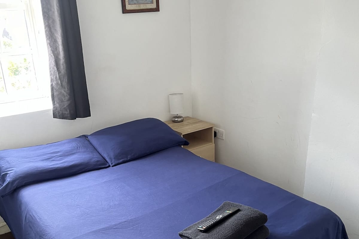 A neatly made bed with blue bedding, a remote control, and a folded towel on it.