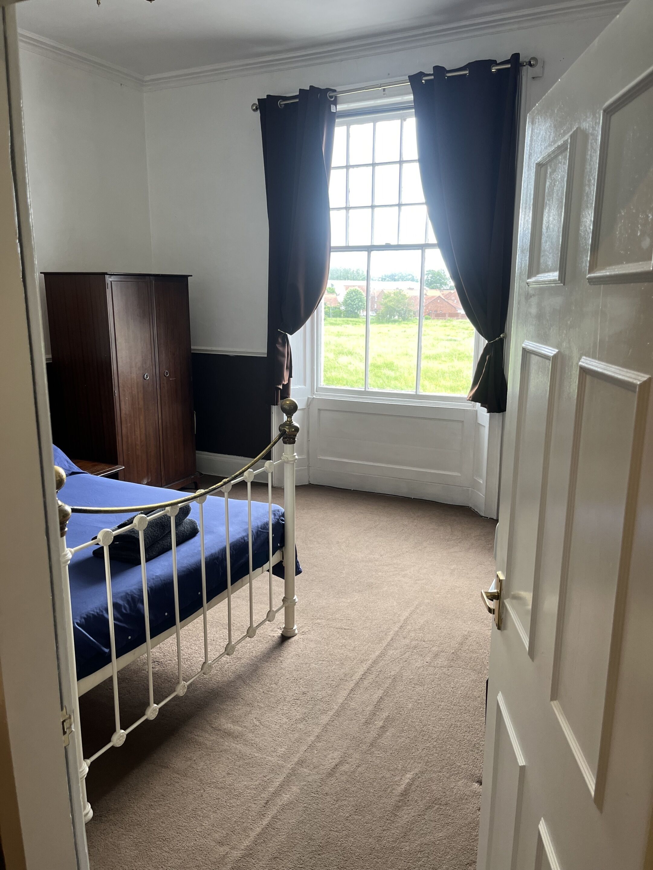 A bedroom with a single bed, a wardrobe, and a window with curtains.