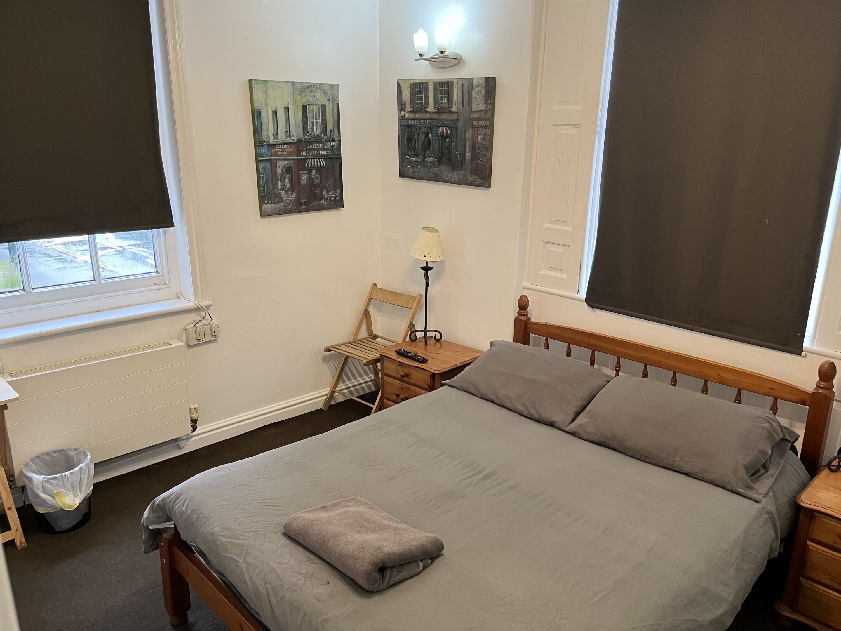 A bedroom with a bed, a chair, a lamp, and two paintings on the wall.