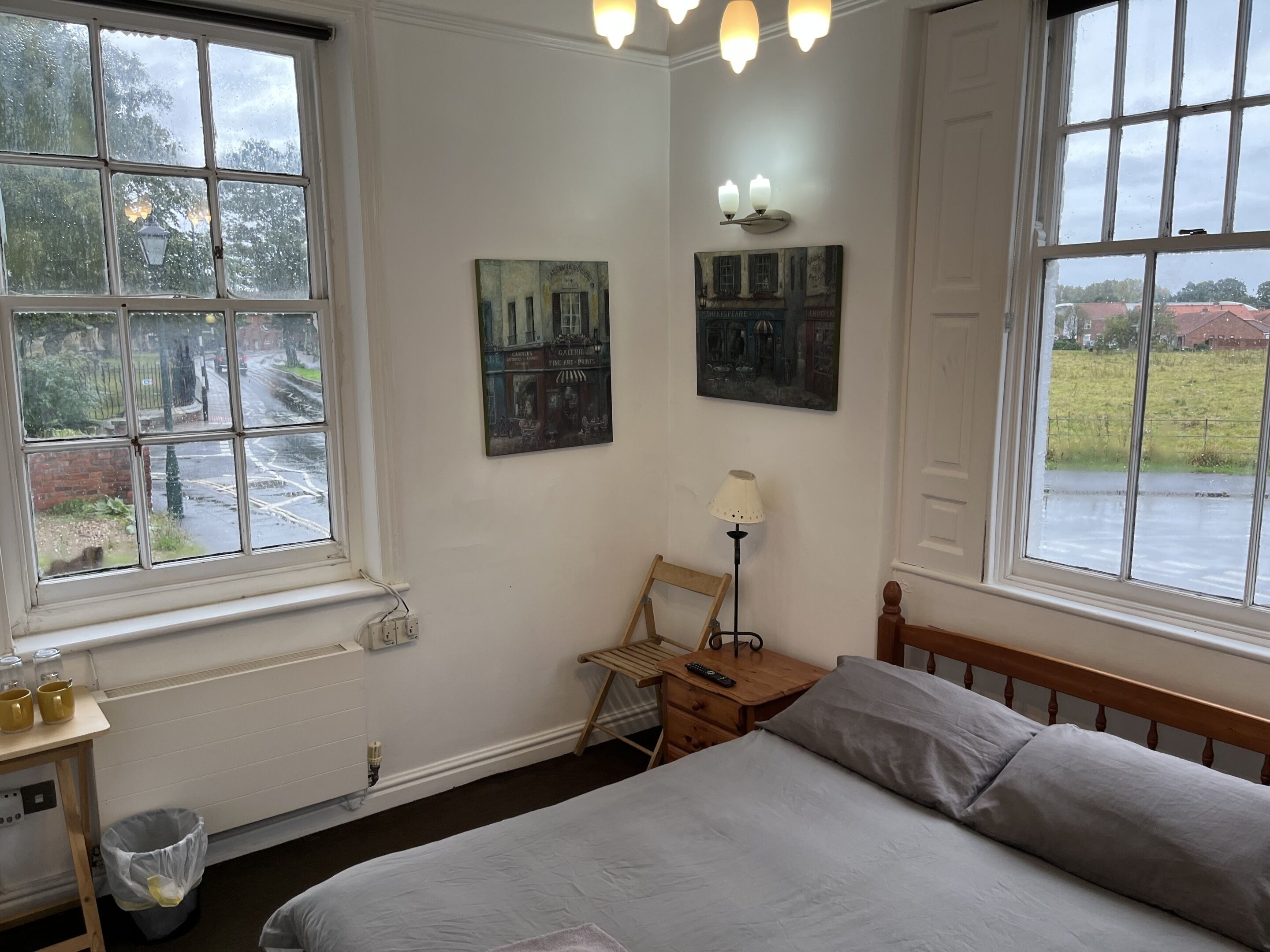 Quarto com cama, mesa de cabeceira, abajur e duas pinturas na parede.