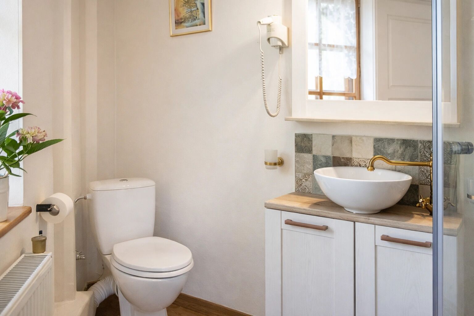 A bathroom with a toilet, a sink with a vessel basin, a mirror, and a wall-mounted telephone.