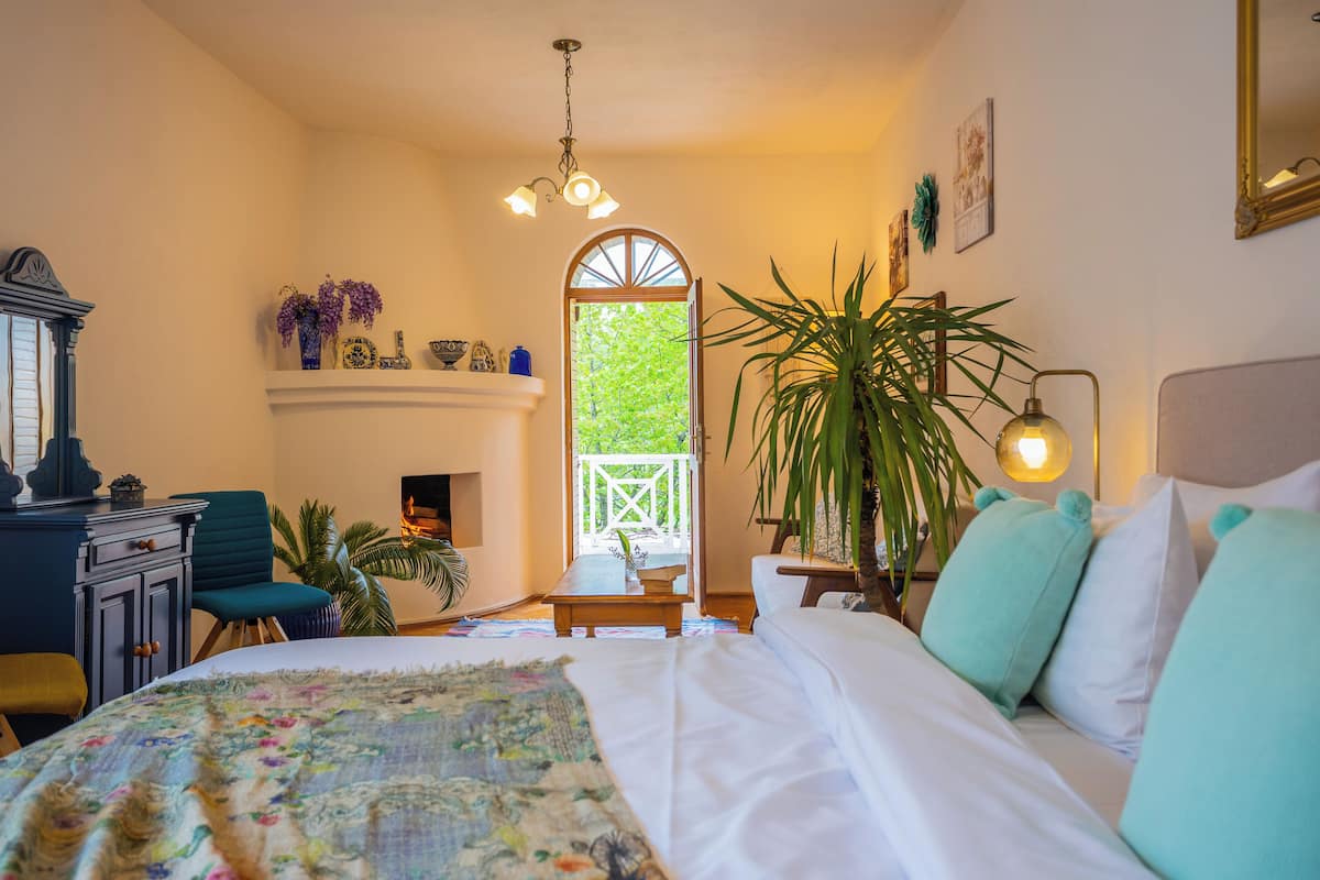 Un dormitorio con cama, escritorio, silla, planta en maceta y ventana con vista a vegetación.