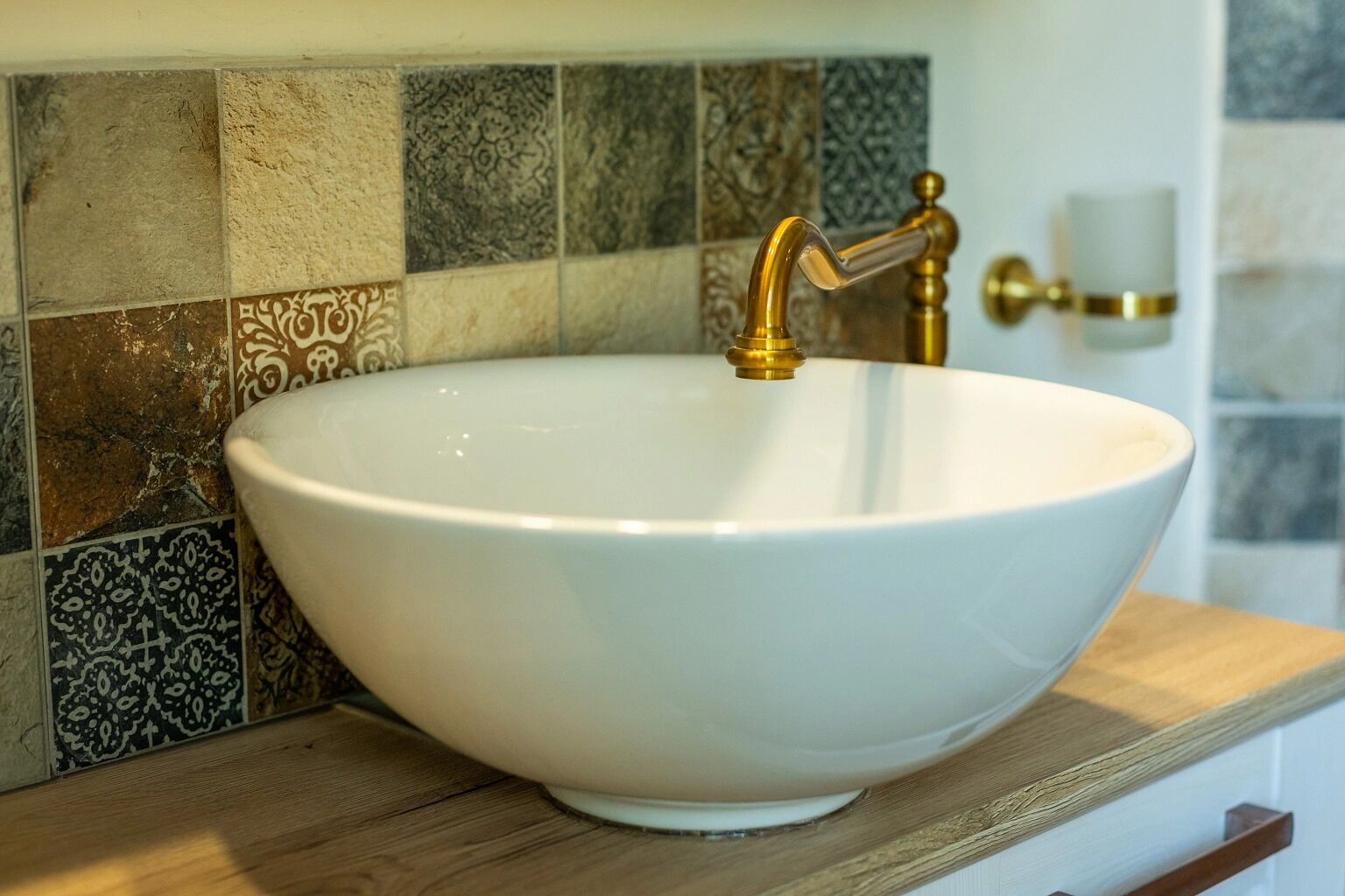 Un lavamanos blanco con grifo dorado sobre una encimera de madera.
