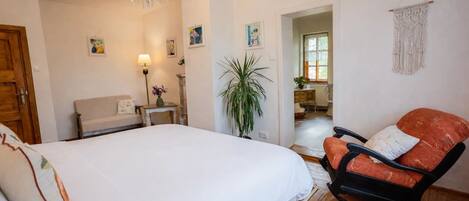A bedroom with a large bed, a rocking chair, a chandelier, and a macrame wall hanging.