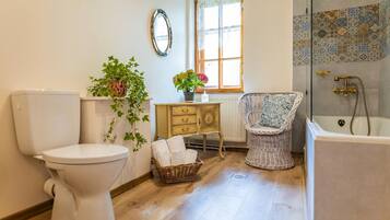 Un baño con inodoro, una silla de mimbre, bañera, ventana y espejo decorativo.
