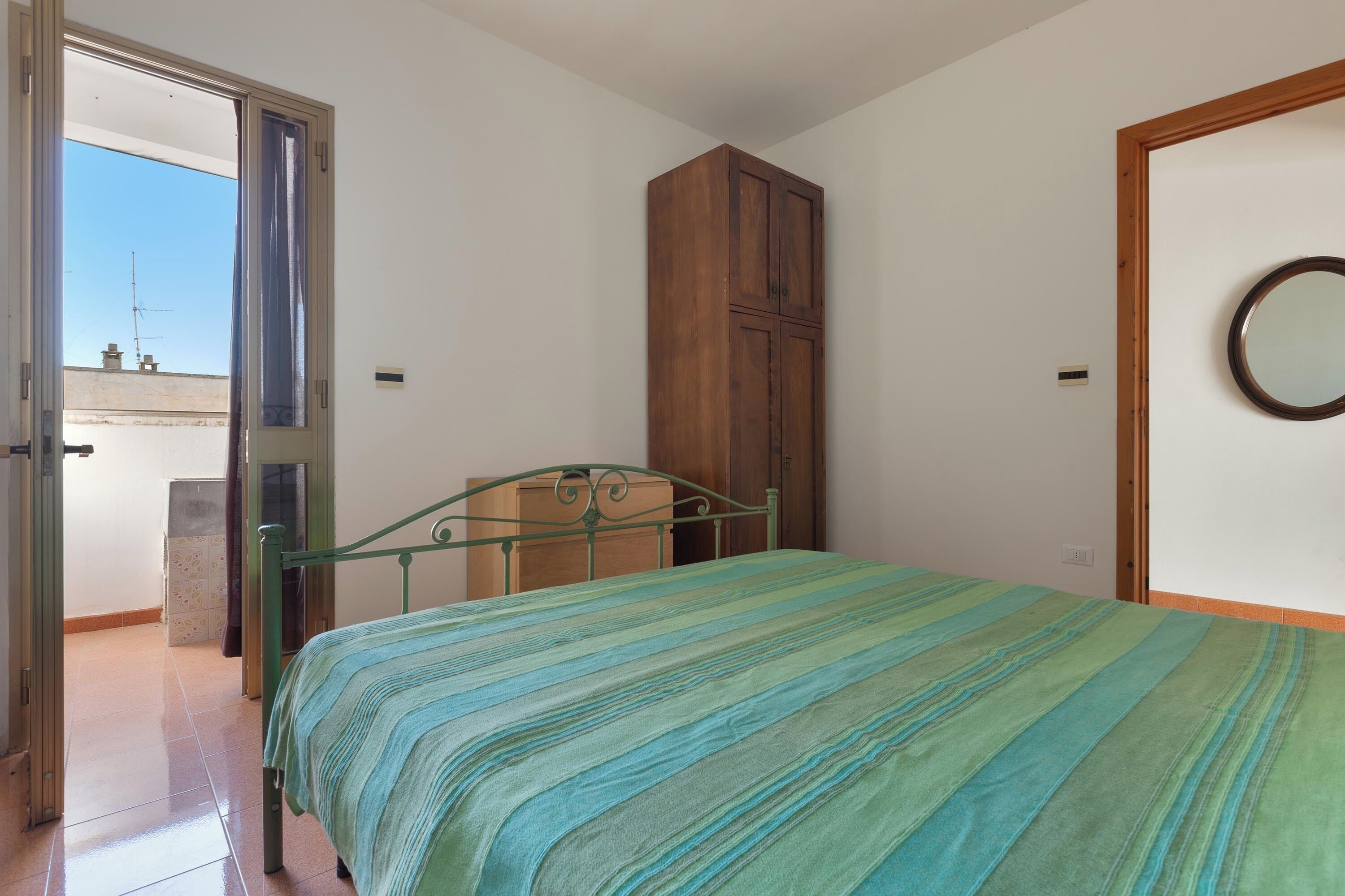 Un dormitorio con cama, armario, puerta con espejo y vistas al exterior.