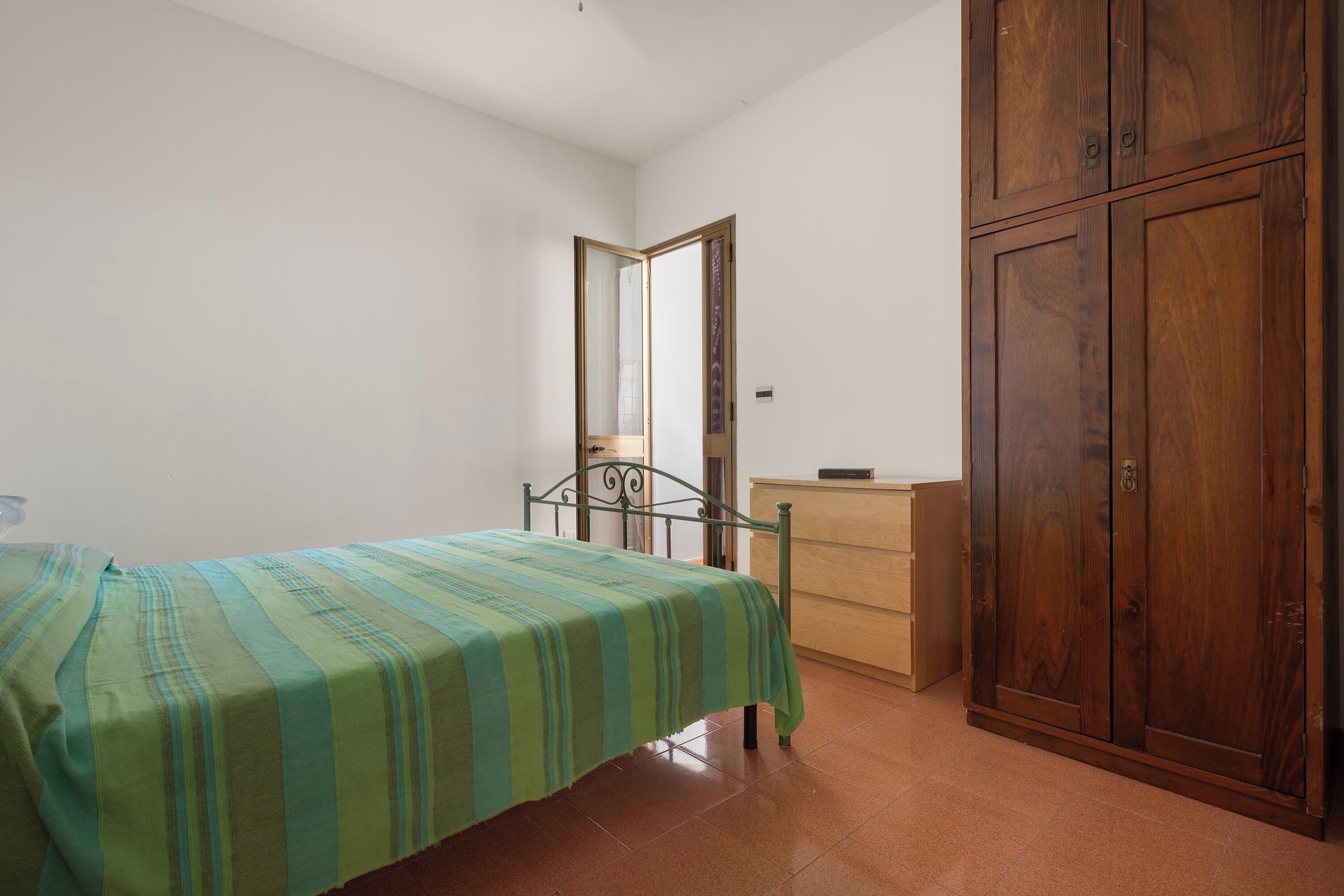 A bedroom with a bed, a wooden wardrobe, and a dresser.