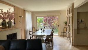 A dining area with a table and chairs, a sofa, and a view of a garden through a large window.
