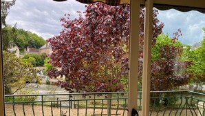 A balcony with a view of a garden, a pond, and a building in the background.