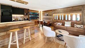 A modern kitchen with wooden accents, a dining area with a round table, and a cozy seating area with a sofa and chairs. - Pilànous Residence - Junior Suite - Swiss Alps (Haute-Nendaz)