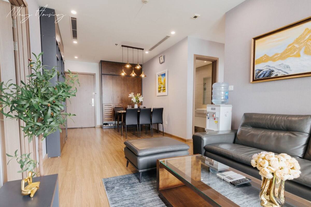 Ein modernes Wohnzimmer mit einem Ledersofa, einem Glastisch und einem Essbereich im Hintergrund.