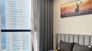 Moderni hotellihuone, jossa on suuri sänky, harmaat vuodevaatteet, harmaa pääty ja ikkunasta avautuva näkymä kaupungin ylle.