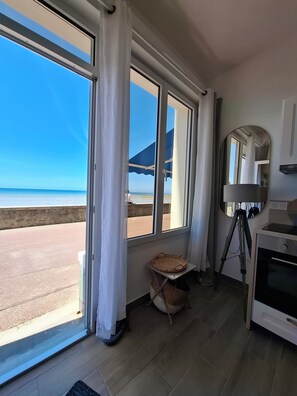A room with a large window, a tripod, a small table, and a cabinet. - Nouveaute : Front DE MER Neuf Bien Équipé Belle VUE MER Pour Sejour Parfait (AGON COUTAINVILLE)