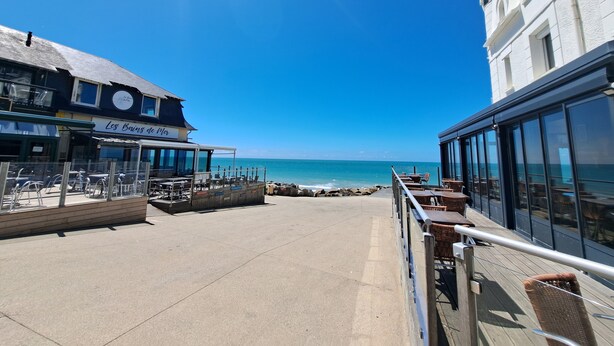 A seaside promenade with outdoor seating, a restaurant named "Les Bains de Mer," and a view of the ocean. - Nouveaute : Front DE MER Neuf Bien Équipé Belle VUE MER Pour Sejour Parfait (AGON COUTAINVILLE)