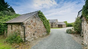 Un edificio de piedra rural con un camino de grava que conduce a otro edificio de piedra.