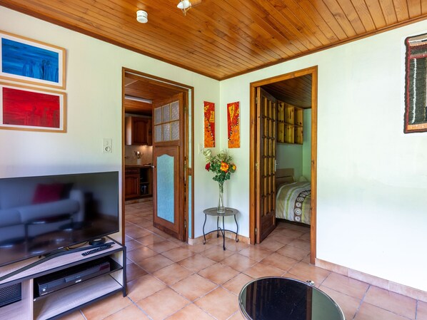 A living room with a TV, a coffee table, and a dining area with a table and chairs. There are doors leading to other rooms.