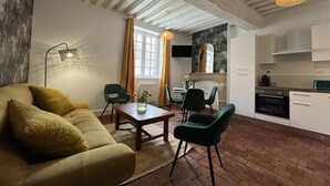 Ein gemütliches Wohnzimmer mit Sofa, Sesseln, einem Couchtisch und einem Essbereich mit Tisch und Stühlen. Es gibt eine Küchenzeile mit Schränken und einem Herd.