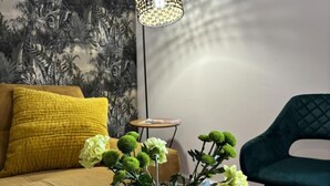 Ein Wohnzimmer mit einer Couch, einem Couchtisch mit Blumen in einer Vase, einer Lampe und einem Sessel.