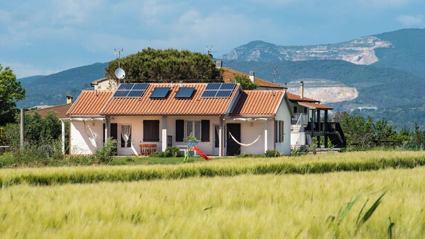 Una casa con techo de tejas, paneles solares y vistas a montañas.